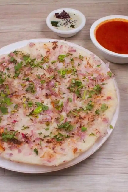 Thick South Indian uttapam pancake topped with onions and herbs, served with chutneys.