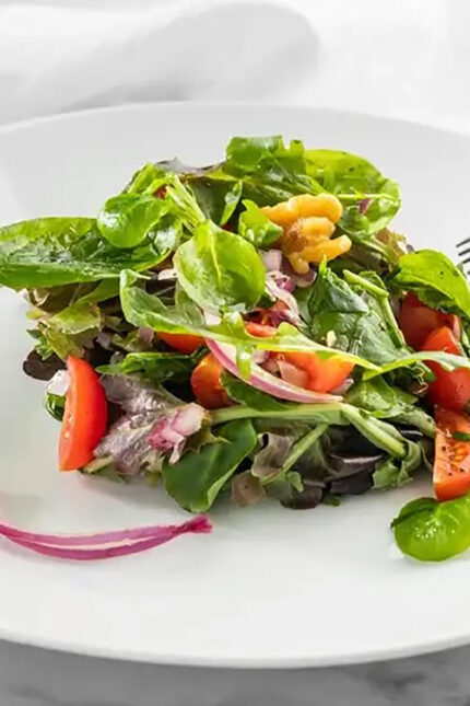 Fresh green salad tossed with walnuts, red onion, and tomatoes at Zari Crawley vegan restaurant.
